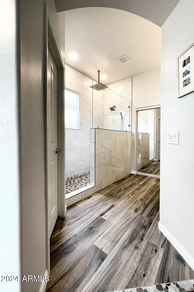 bathroom featuring hardwood / wood-style floors, a tile shower, and tile walls