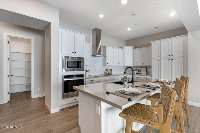 kitchen with a center island with sink, wall chimney range hood, white cabinets, appliances with stainless steel finishes, and sink