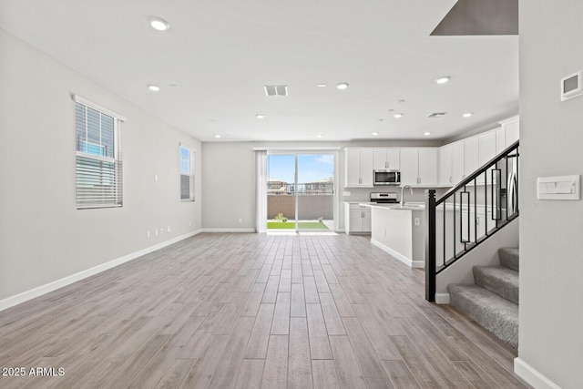 21047 N 58th Way, Phoenix, AZ 85054 - unfurnished living room with light wood-style flooring, baseboards, stairway, a sink, and recessed lighting