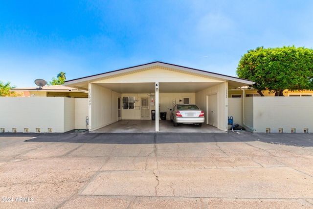 view of parking with driveway, an attached carport, and fence