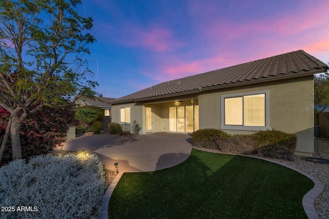 back house at dusk featuring a patio, central AC, and a lawn