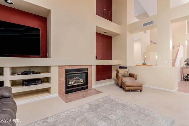 carpeted living room with built in features, a tile fireplace, and a high ceiling