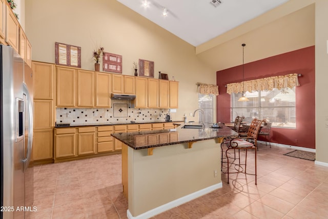 kitchen featuring stainless steel refrigerator with ice dispenser, a kitchen bar, tasteful backsplash, sink, and a kitchen island with sink