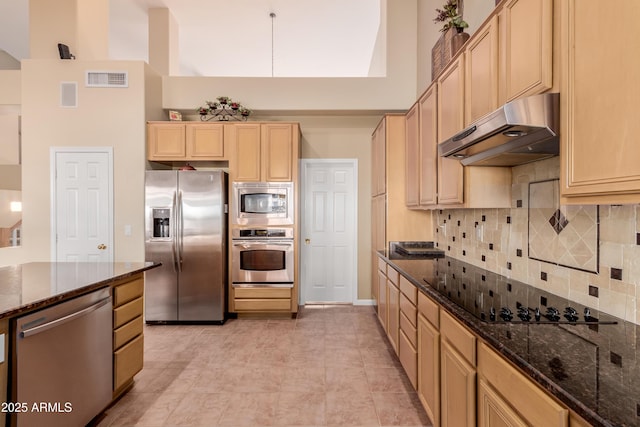 kitchen with decorative backsplash, a high ceiling, stainless steel appliances, light brown cabinetry, and dark stone counters