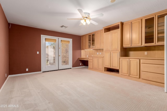 unfurnished living room with built in desk, light carpet, french doors, and ceiling fan