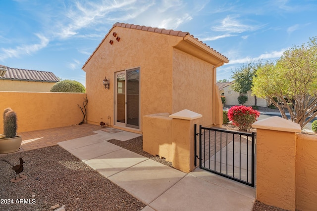 exterior space featuring a tile roof, a gate, fence, and stucco siding