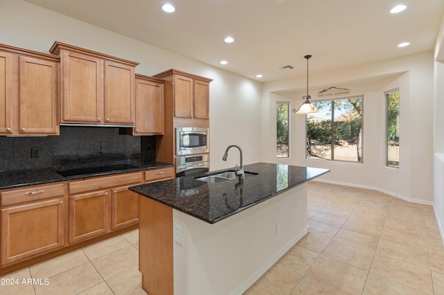 kitchen with appliances with stainless steel finishes, a kitchen island with sink, dark stone countertops, and sink