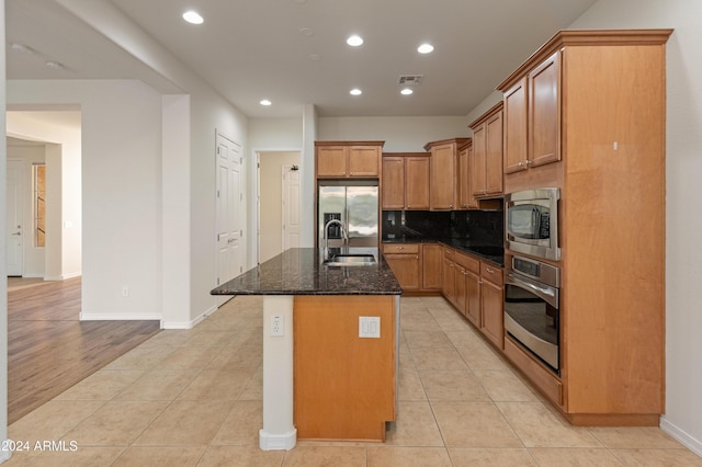 kitchen with a kitchen island with sink, sink, dark stone countertops, appliances with stainless steel finishes, and light tile patterned flooring