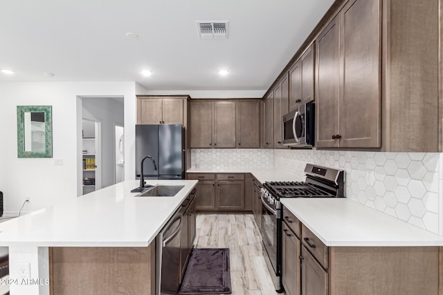 kitchen with light wood-type flooring, stainless steel appliances, an island with sink, and sink