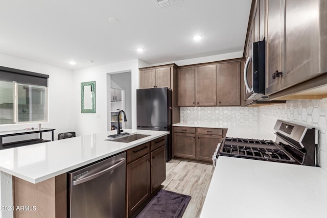 kitchen with decorative backsplash, stainless steel appliances, sink, a center island with sink, and light hardwood / wood-style flooring