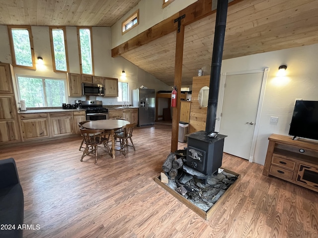 interior space featuring appliances with stainless steel finishes, wood ceiling, high vaulted ceiling, light hardwood / wood-style flooring, and a wood stove