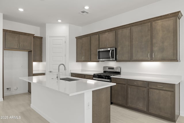 kitchen with visible vents, dark brown cabinets, a center island with sink, a sink, and stainless steel appliances
