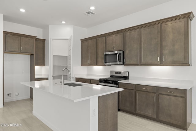kitchen featuring visible vents, dark brown cabinetry, a center island with sink, a sink, and stainless steel appliances
