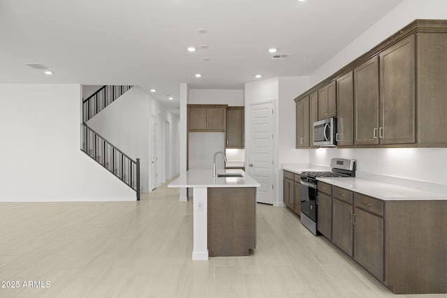 kitchen with recessed lighting, a sink, appliances with stainless steel finishes, and a center island with sink