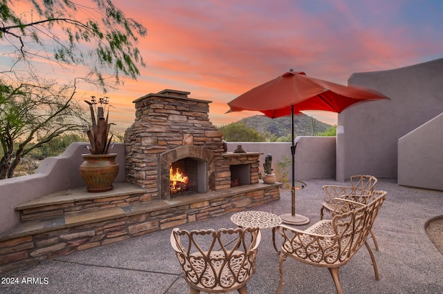 patio terrace at dusk featuring an outdoor stone fireplace and a mountain view