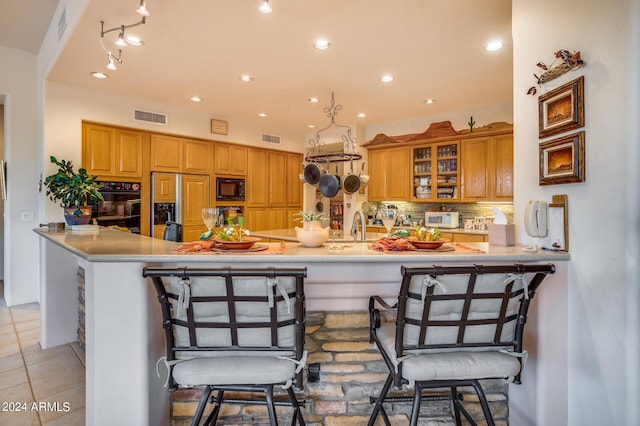 kitchen featuring sink, kitchen peninsula, a kitchen bar, light tile patterned flooring, and black appliances