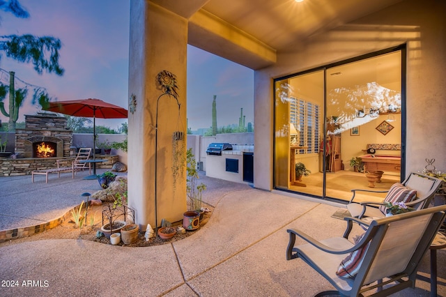 patio terrace at dusk featuring an outdoor stone fireplace, area for grilling, and grilling area