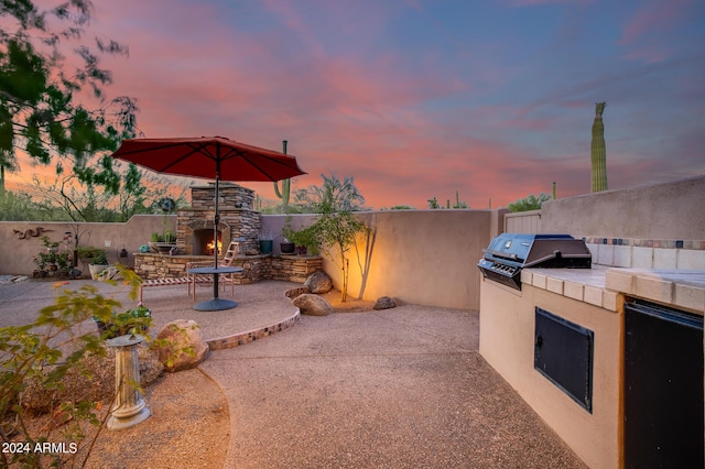 patio terrace at dusk featuring a grill, exterior kitchen, and an outdoor stone fireplace