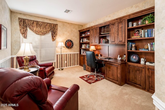 office area featuring a wainscoted wall, light colored carpet, visible vents, built in study area, and wallpapered walls