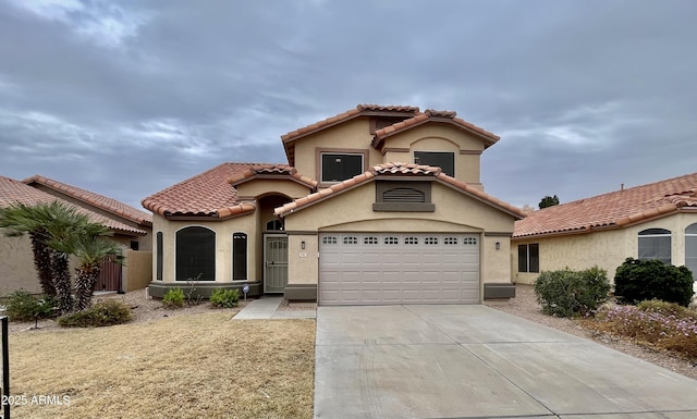 mediterranean / spanish-style house featuring a garage, concrete driveway, a tiled roof, and stucco siding