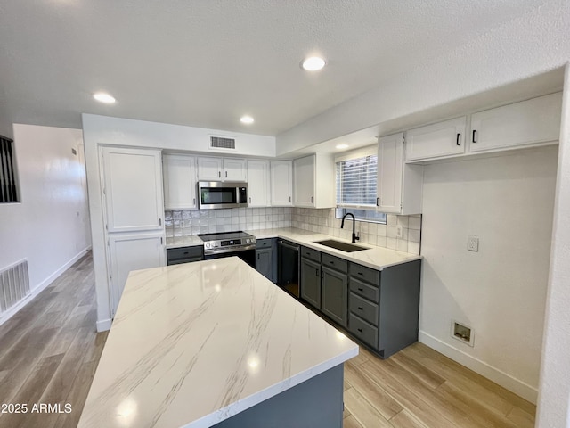 kitchen featuring tasteful backsplash, sink, light stone counters, stainless steel appliances, and light wood-type flooring