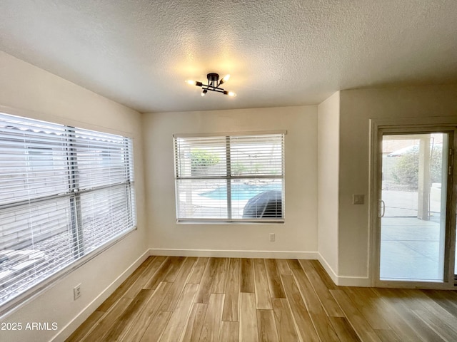 unfurnished room with plenty of natural light, a textured ceiling, and light wood-type flooring