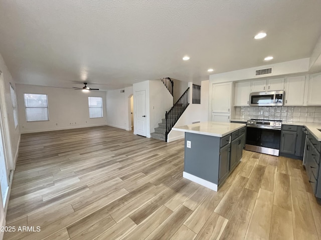 kitchen with tasteful backsplash, a center island, light wood-type flooring, stainless steel appliances, and white cabinets