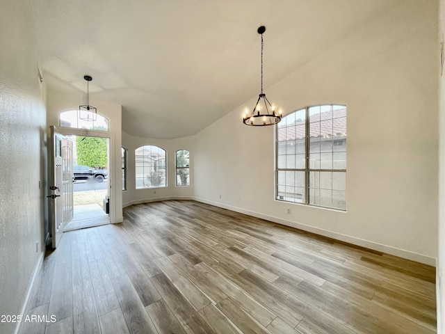 unfurnished dining area with an inviting chandelier, lofted ceiling, and light wood-type flooring