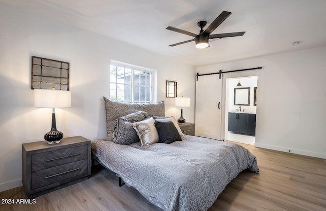 bedroom featuring connected bathroom, ceiling fan, a barn door, and hardwood / wood-style flooring