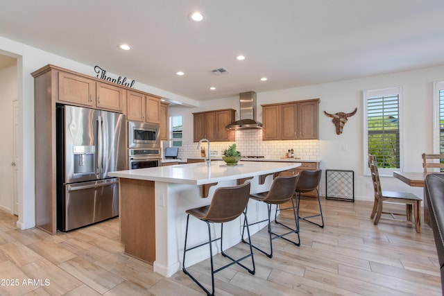 4350 Stage Stop Way, Wickenburg, AZ 85390 - kitchen with appliances with stainless steel finishes, wall chimney range hood, a kitchen island with sink, decorative backsplash, and light countertops