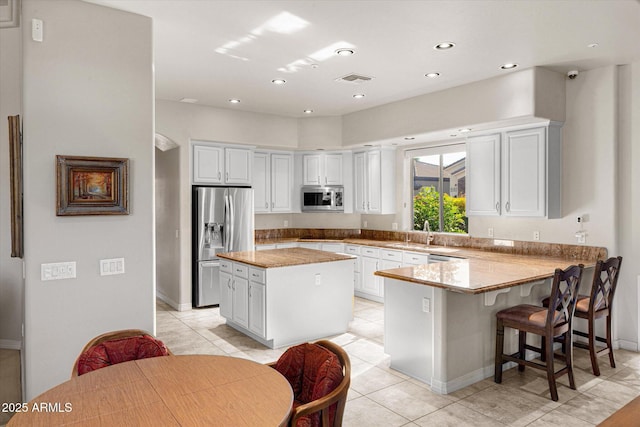 kitchen featuring white cabinets, appliances with stainless steel finishes, a center island, kitchen peninsula, and light tile patterned flooring