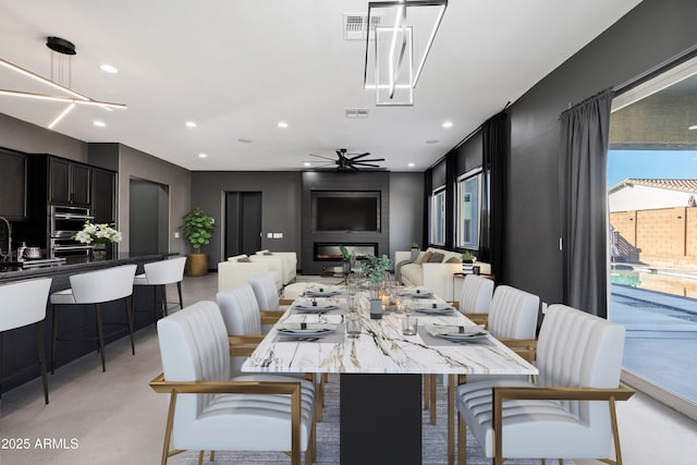 dining space featuring ceiling fan, a large fireplace, and sink