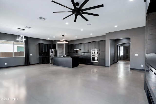 kitchen featuring tasteful backsplash, concrete flooring, stainless steel appliances, a kitchen island with sink, and ceiling fan