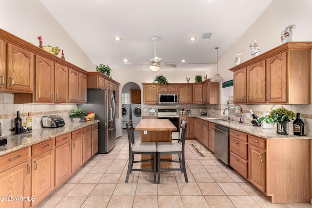 kitchen featuring light tile patterned floors, a kitchen island, ceiling fan, stainless steel appliances, and washer and clothes dryer