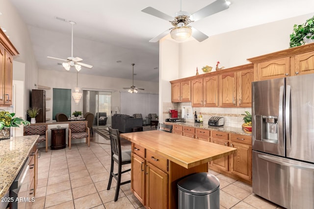 kitchen with light tile patterned floors, butcher block counters, a center island, stainless steel fridge with ice dispenser, and decorative backsplash