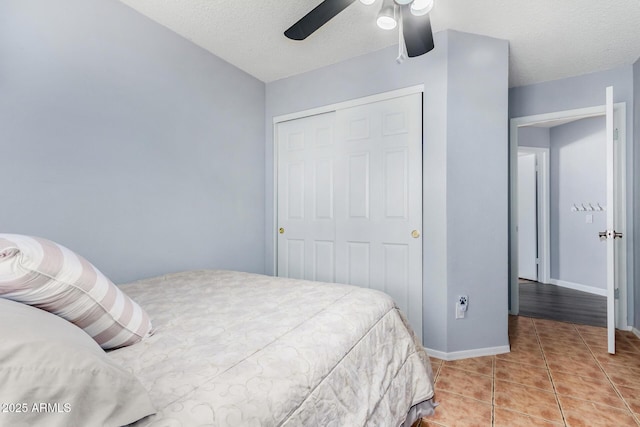 bedroom with a ceiling fan, a textured ceiling, a closet, light tile patterned flooring, and baseboards