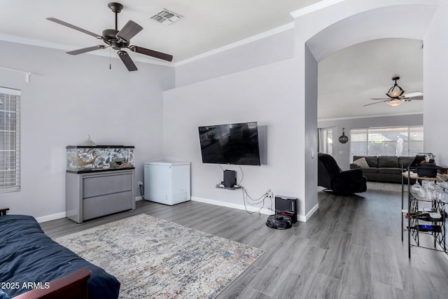 living room featuring wood finished floors, baseboards, visible vents, ornamental molding, and ceiling fan