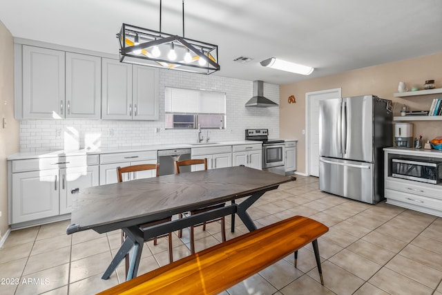 kitchen featuring sink, wall chimney exhaust hood, light tile patterned floors, hanging light fixtures, and appliances with stainless steel finishes