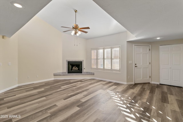 unfurnished living room with ceiling fan, a tile fireplace, and hardwood / wood-style floors