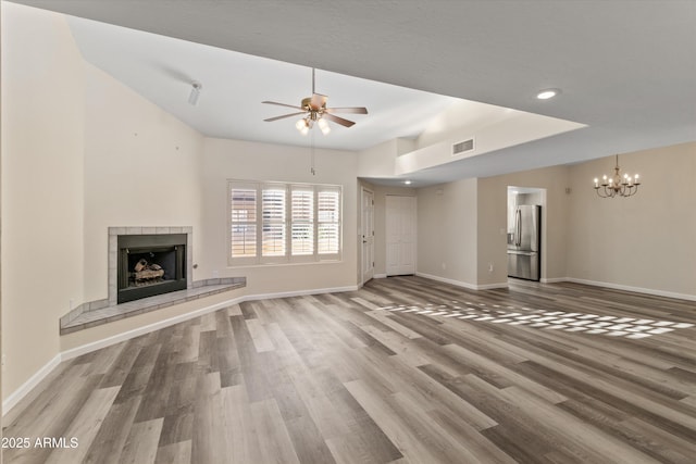 unfurnished living room with ceiling fan with notable chandelier, hardwood / wood-style floors, and a fireplace