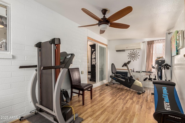 exercise area with a wall unit AC, brick wall, a ceiling fan, and wood finished floors