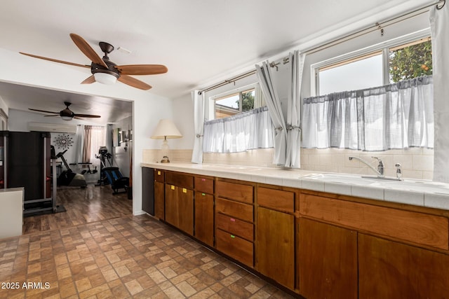 kitchen with tile countertops, brick floor, a sink, brown cabinets, and tasteful backsplash