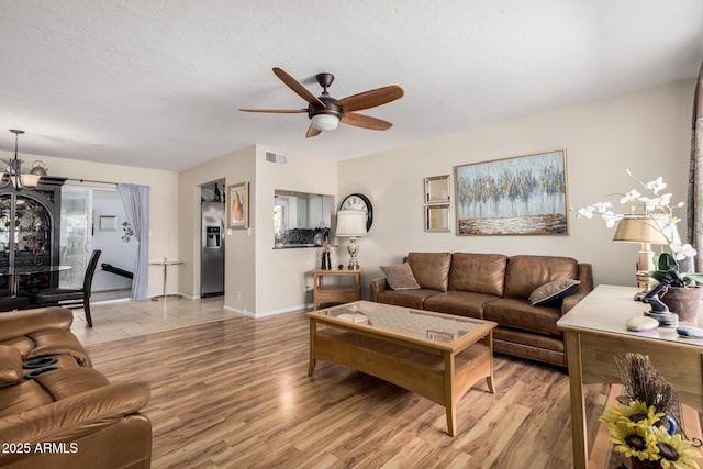 living room with ceiling fan with notable chandelier, light wood-type flooring, visible vents, and baseboards