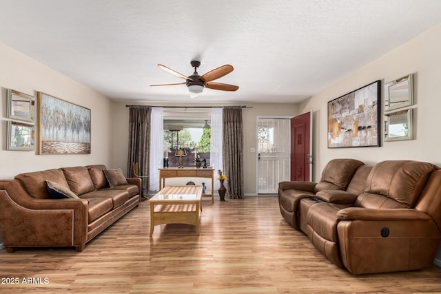 living area featuring light wood-type flooring, ceiling fan, and a textured ceiling