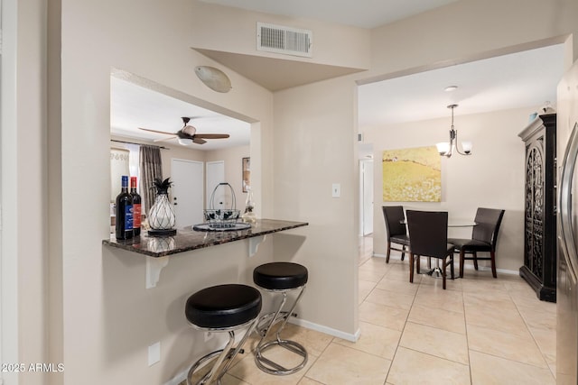 kitchen featuring light tile patterned floors, visible vents, a ceiling fan, dark stone counters, and a kitchen bar