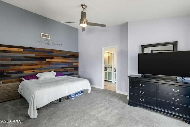 bedroom with ceiling fan, connected bathroom, light colored carpet, and wooden walls