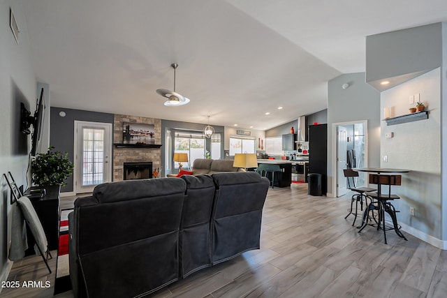 living room with a stone fireplace, vaulted ceiling, and light hardwood / wood-style floors