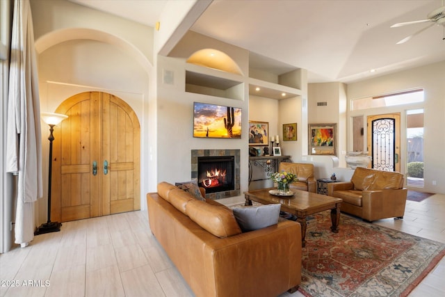 living room featuring ceiling fan, a tiled fireplace, and high vaulted ceiling