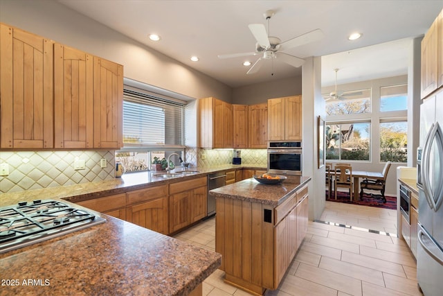 kitchen featuring appliances with stainless steel finishes, sink, decorative backsplash, a center island, and ceiling fan