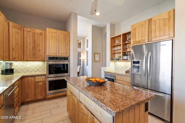 kitchen with ceiling fan, appliances with stainless steel finishes, backsplash, a center island, and light stone countertops